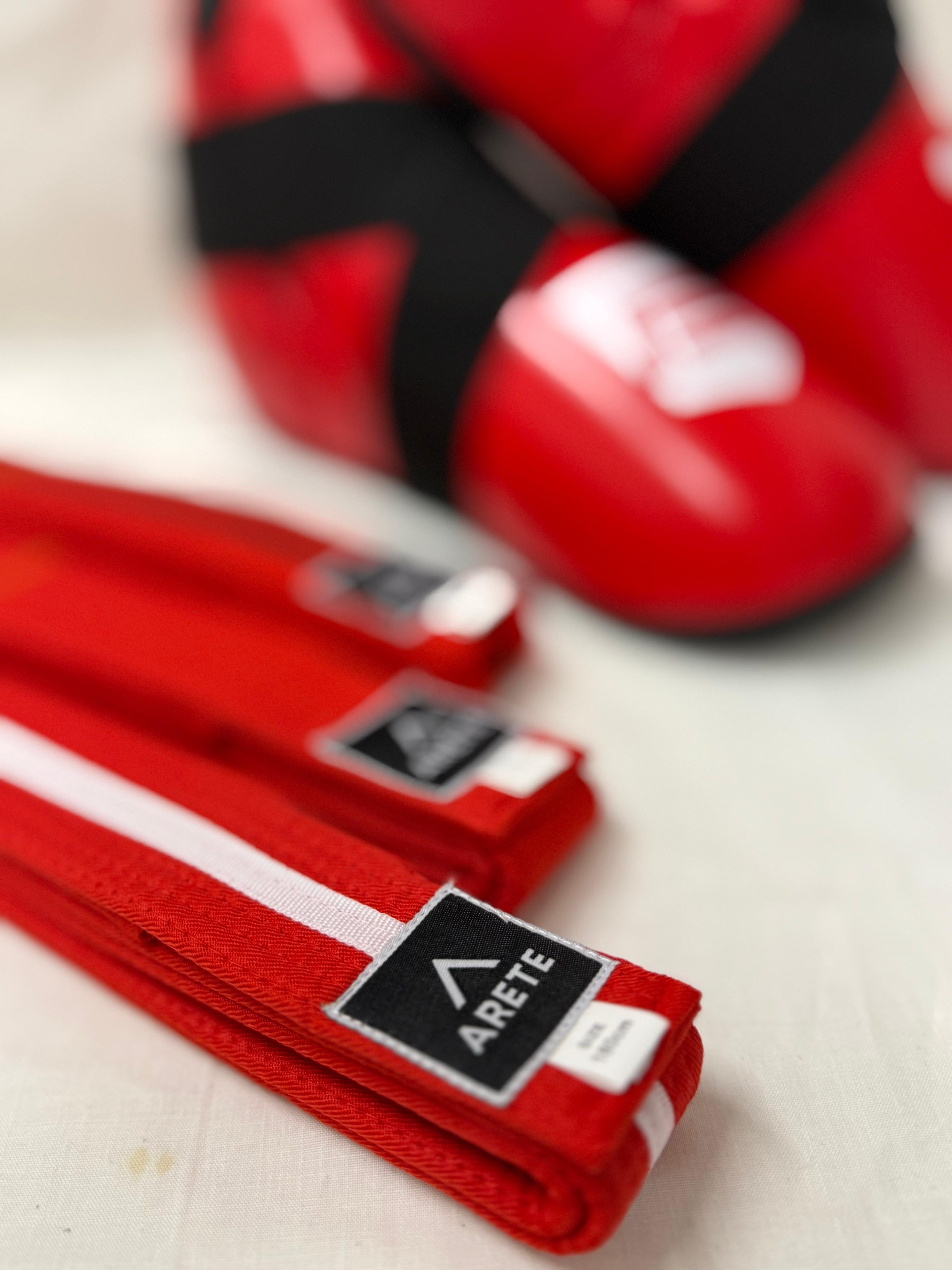 Red martial arts belts with Arete logo on a light background