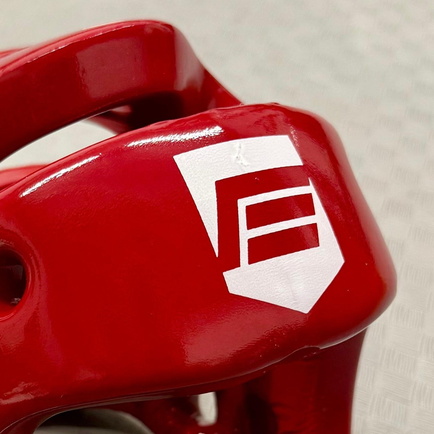 Red protective headgear with a logo on a grey textured background