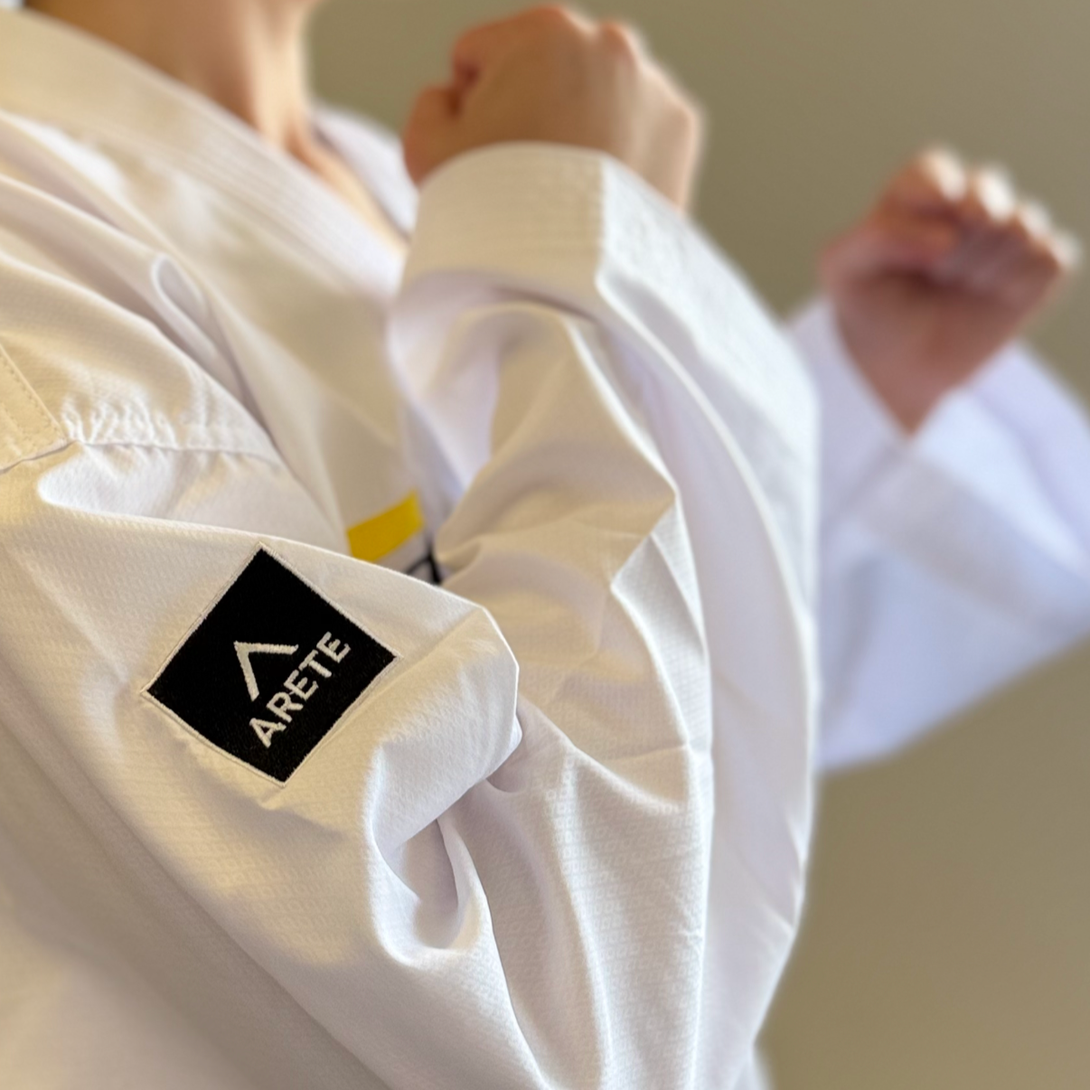 Person wearing a white martial arts uniform with 'Arete' logo on sleeve.