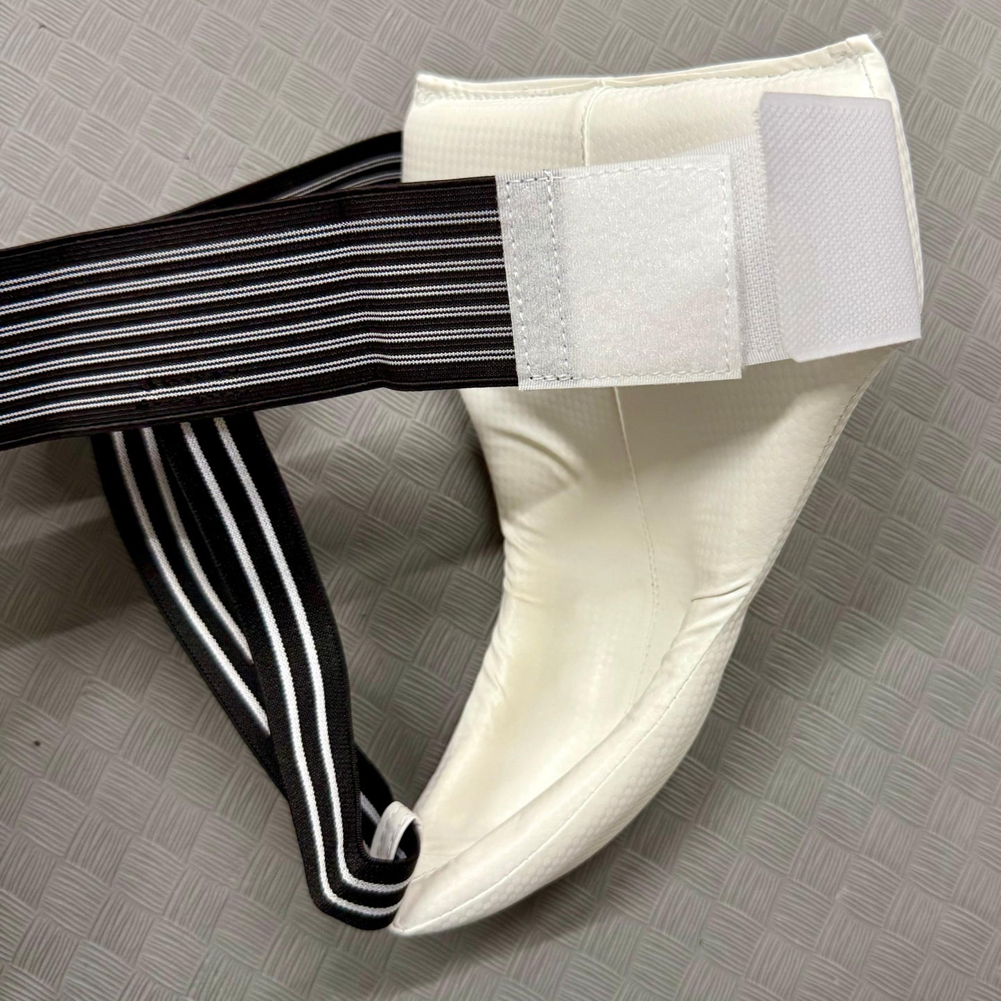 White groin guard black and white striped strap on a grey textured surface
