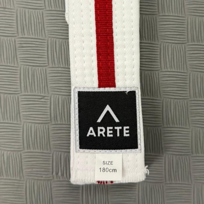 White belt with red stripe on a textured gray mat, featuring the Arete brand logo.
