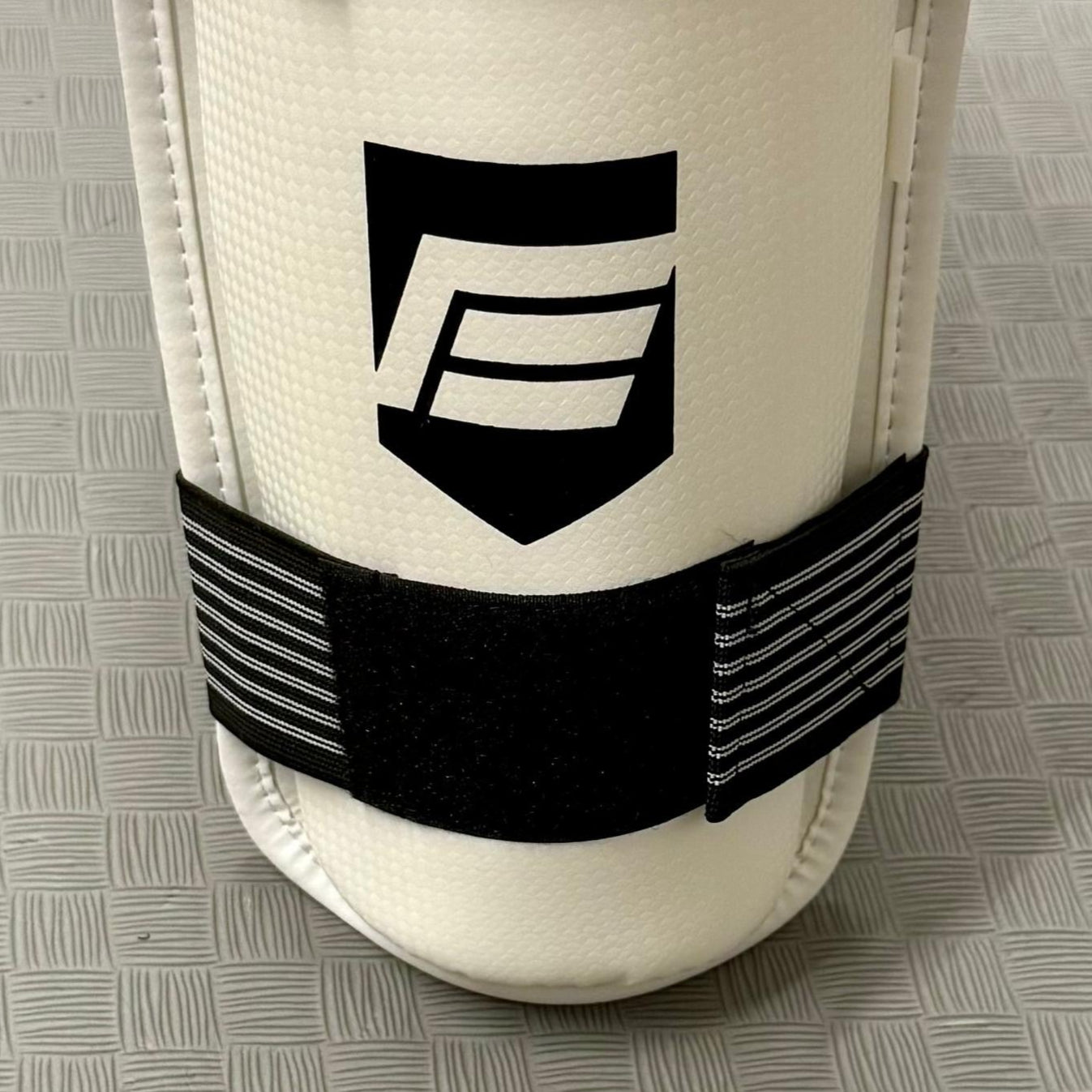White shin guard with black strap on a grey mat