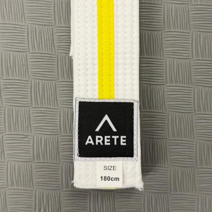 White belt with yellow stripe and Arete logo on a textured gray background