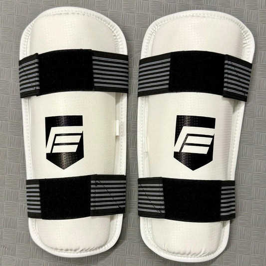 Pair of white shin guards with black straps on a grey background