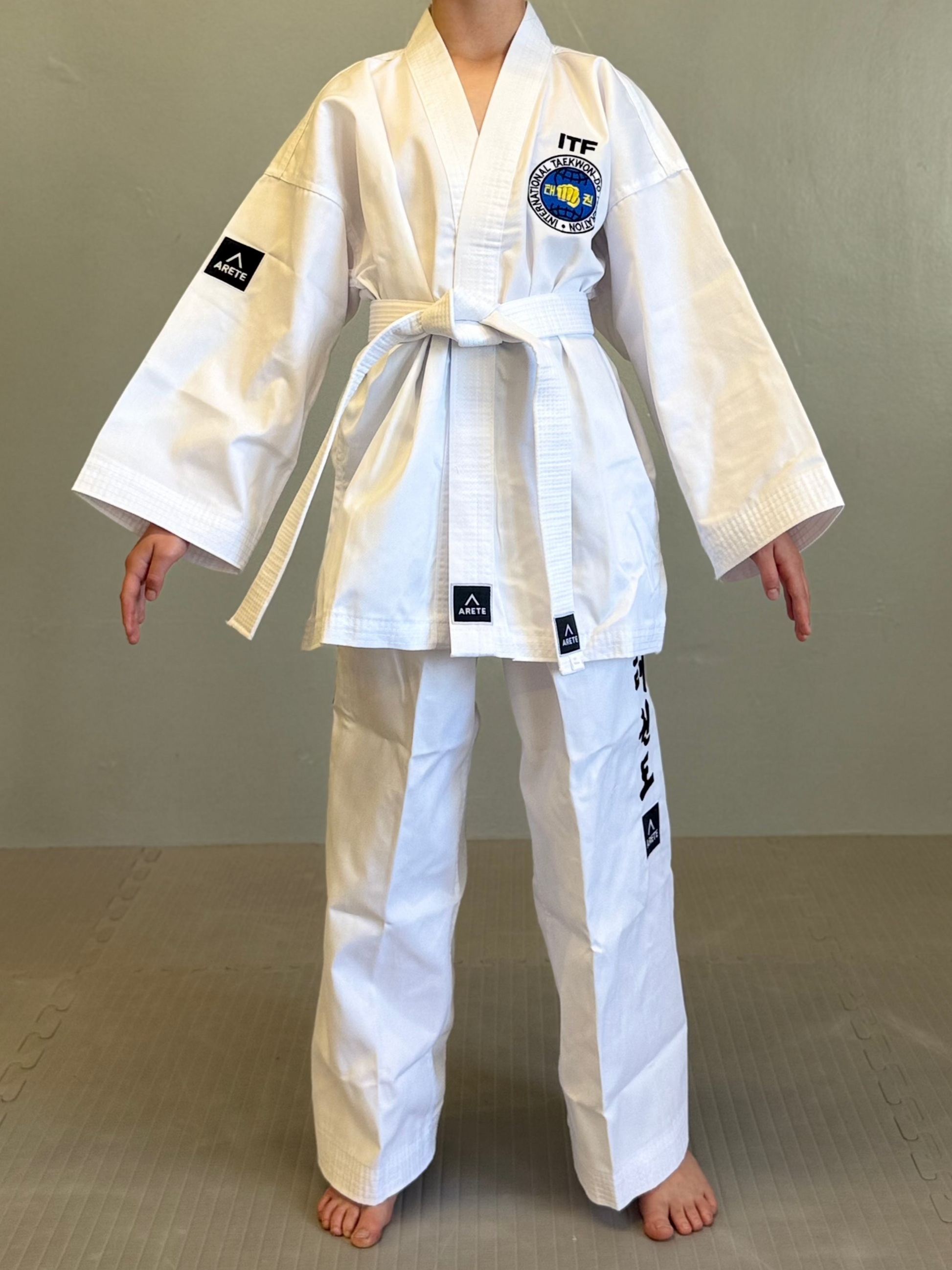 Person wearing a white martial arts uniform with ITF logo on a gray background