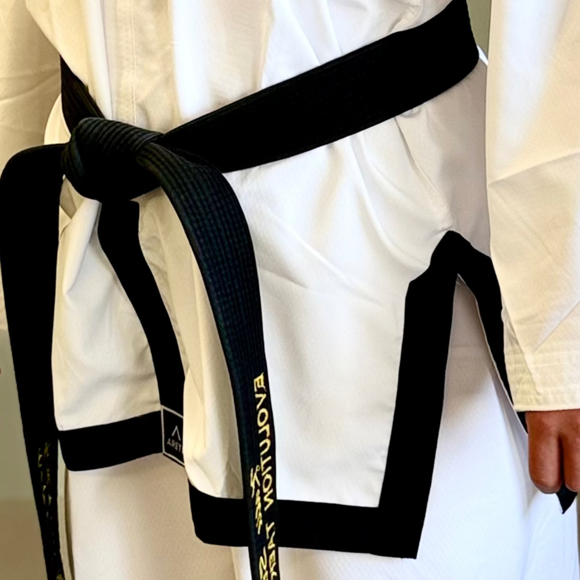 Person wearing a white martial arts uniform with a black belt featuring a brand logo.