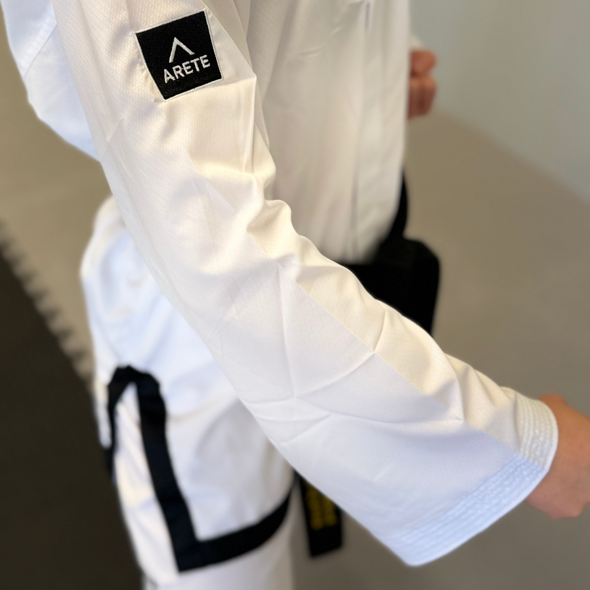 Person wearing a white martial arts uniform with Arete logo on sleeve