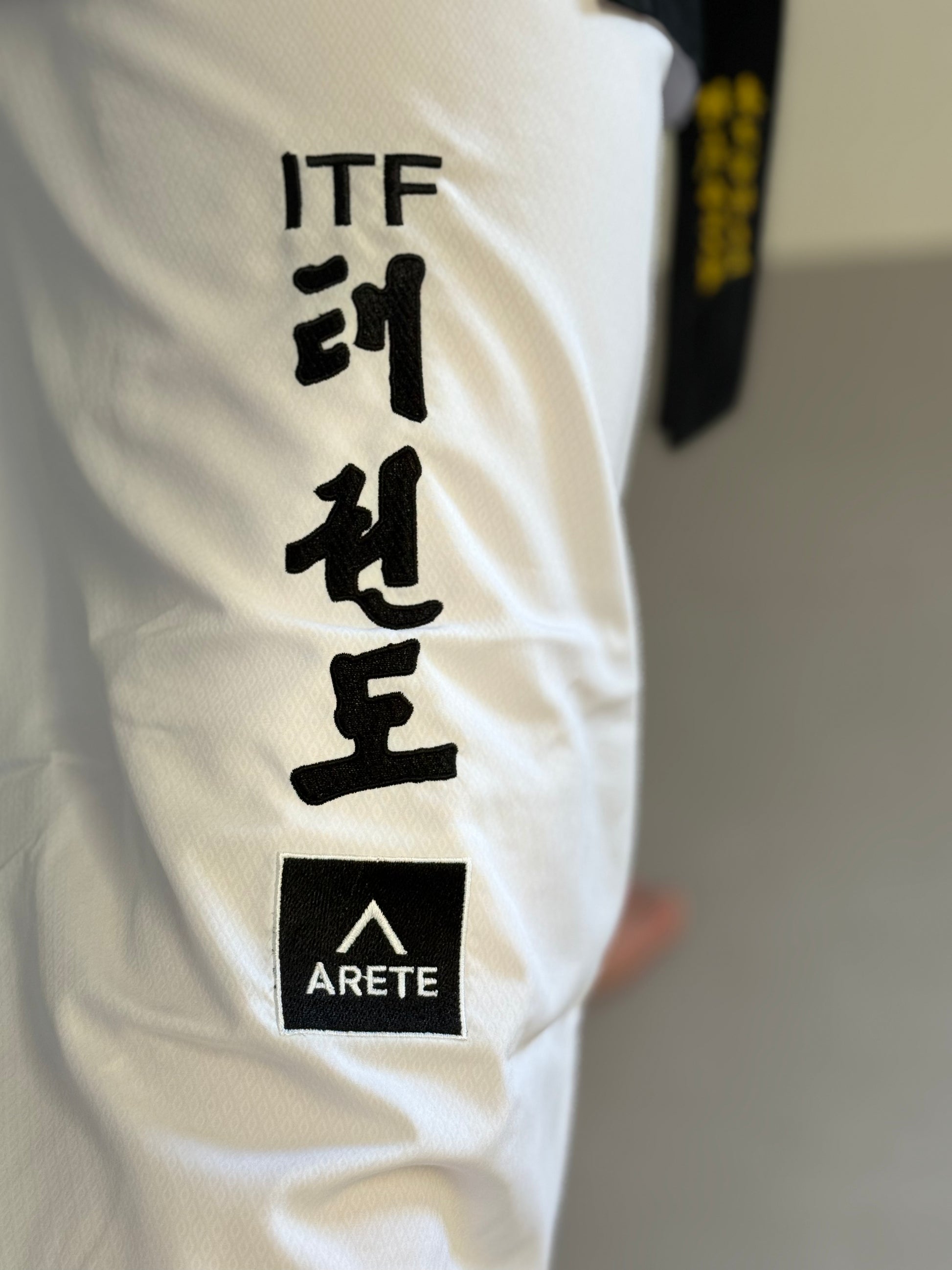 White martial arts uniform with black text and Arete logo on a blurred background