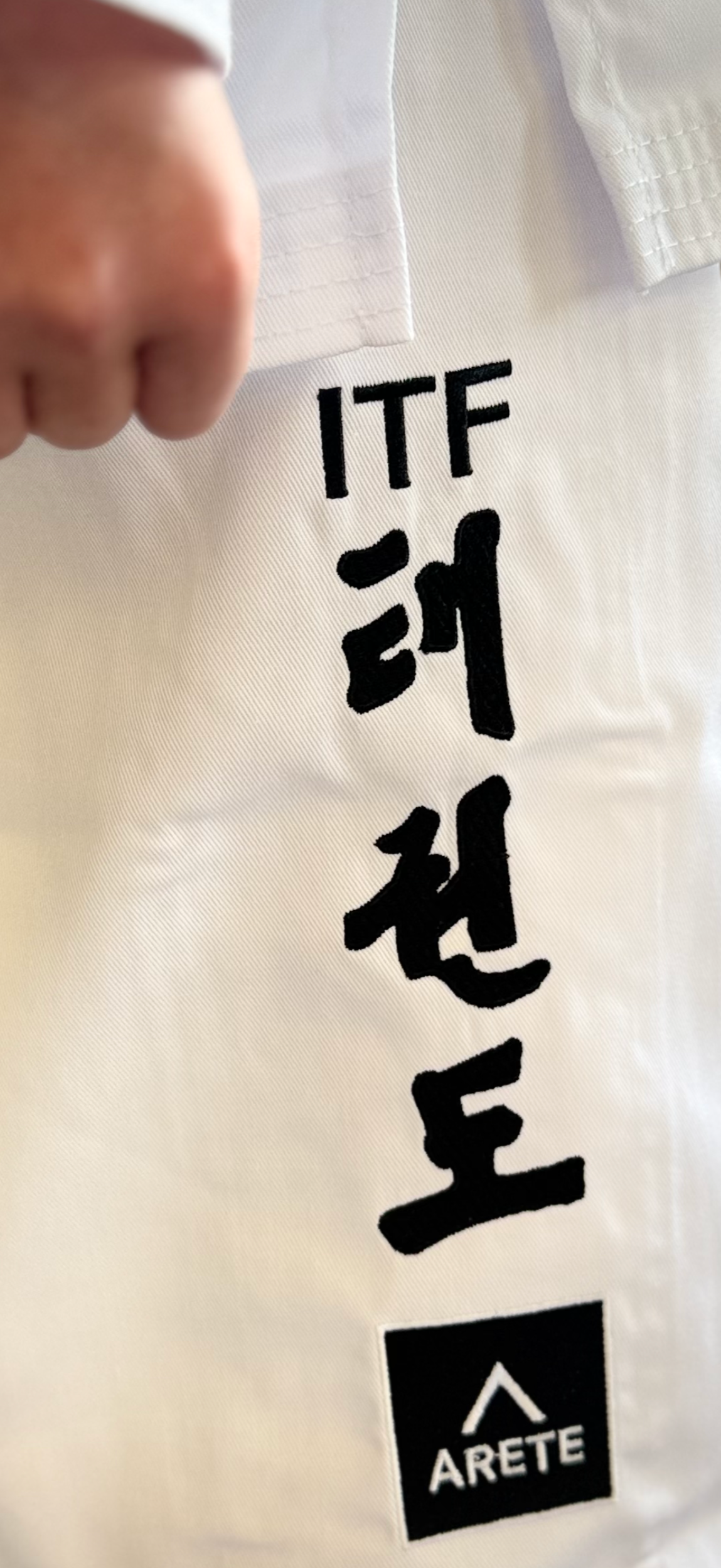 White martial arts uniform with 'ITF' and 'ARETE' branding held by a hand.