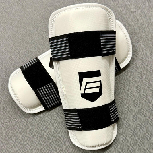 White shin guards with black straps on a grey mat
