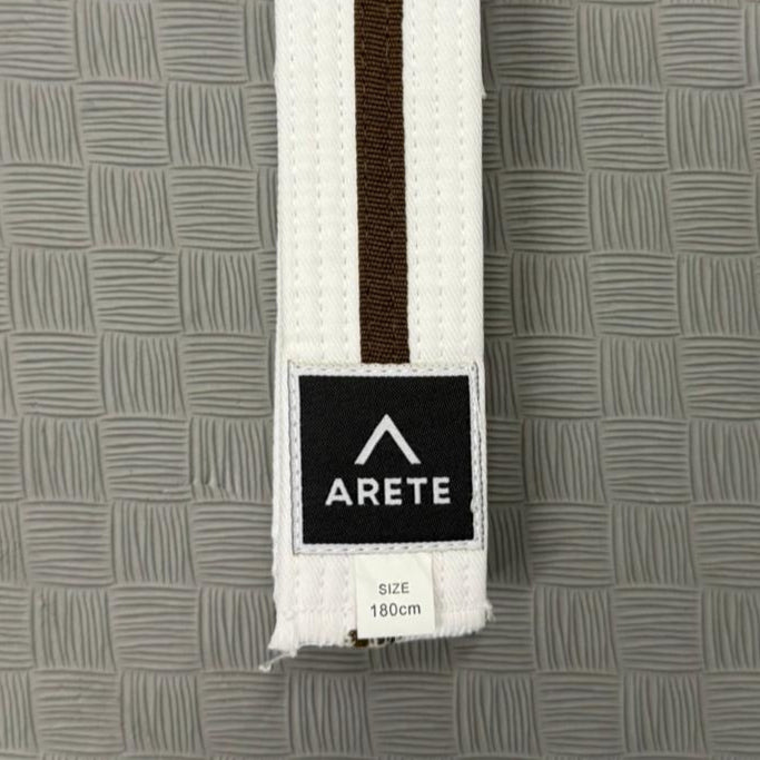 White belt with a brown stripe on a textured gray background, featuring the Arete brand logo.