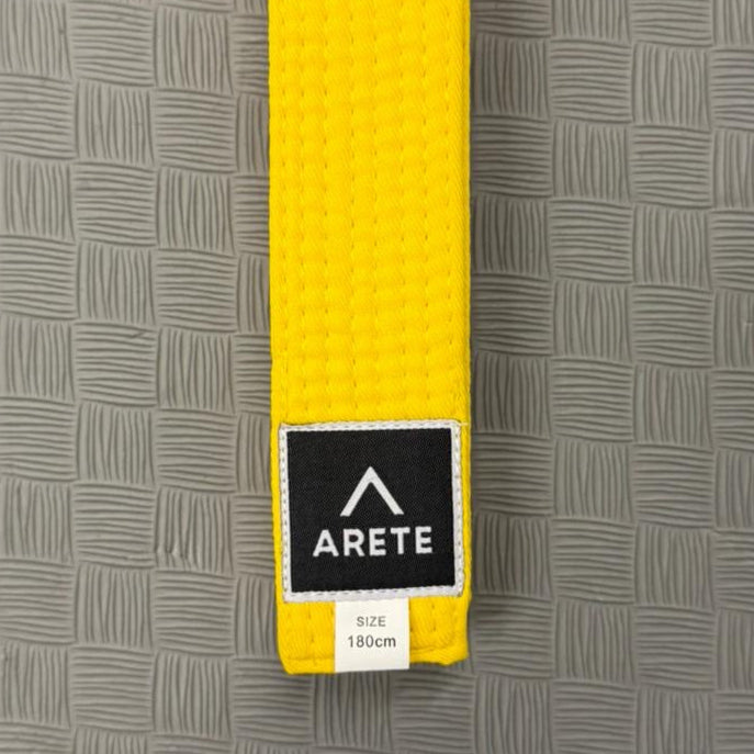 Yellow belt with Arete logo on a gray textured background
